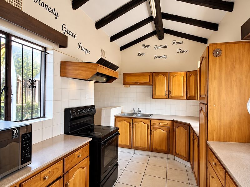 A functional kitchen featuring wooden cabinetry, laminate countertops, a double basin sink, and exposed timber ceiling beams, complemented by tiled flooring.