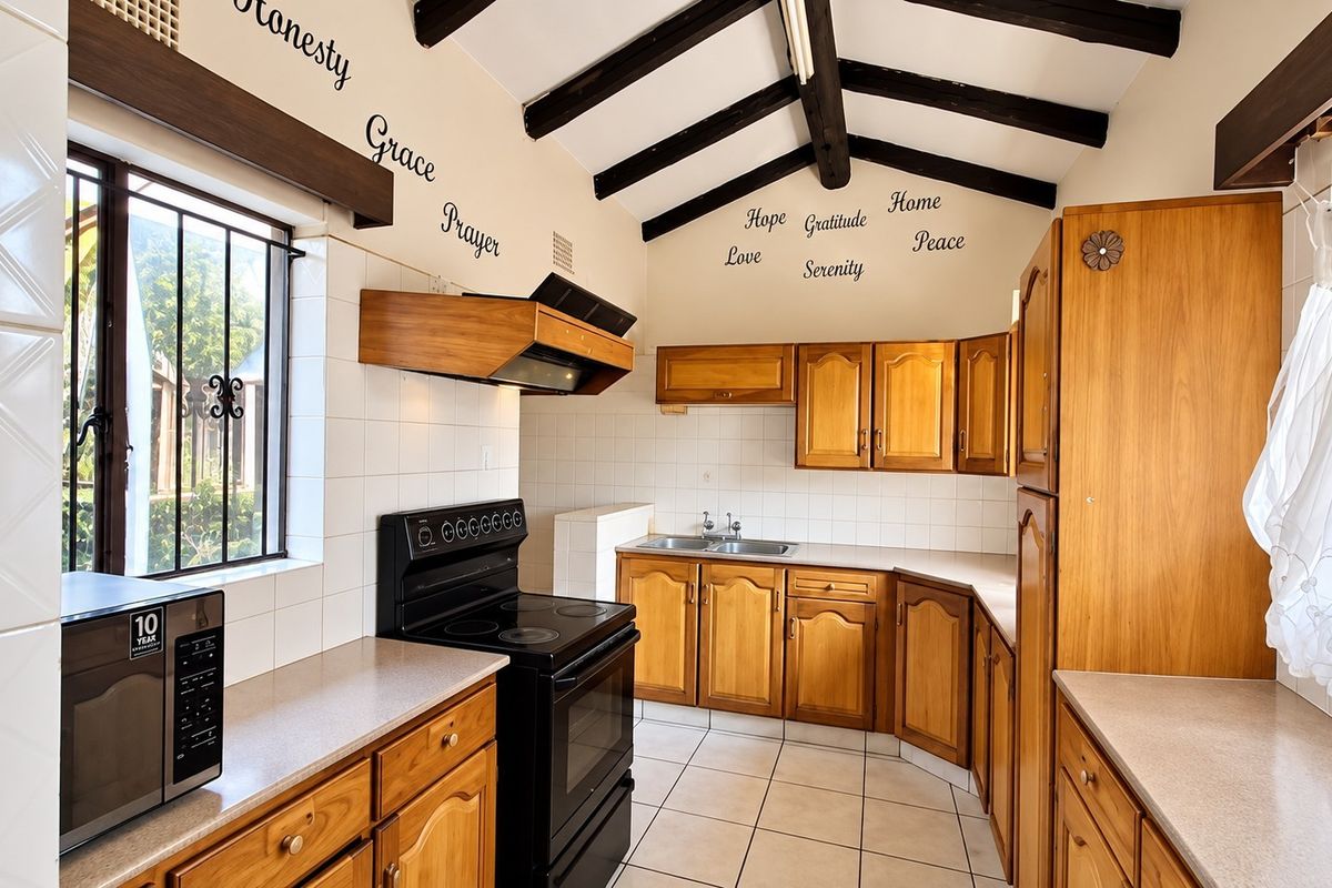 A functional kitchen featuring wooden cabinetry, laminate countertops, a double basin sink, and exposed timber ceiling beams, complemented by tiled flooring.