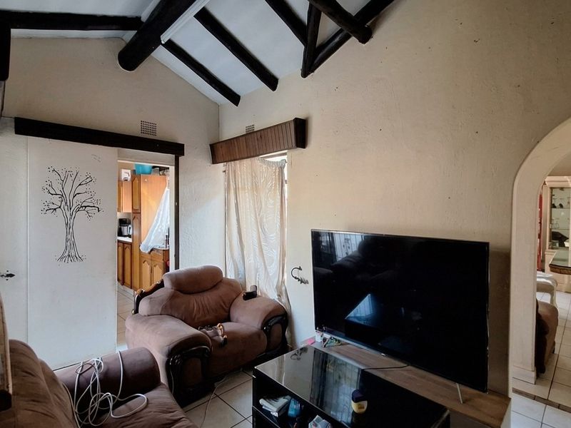 Living room featuring a vaulted ceiling with exposed timber beams, tiled flooring, and an arched entryway leading to adjacent living spaces.