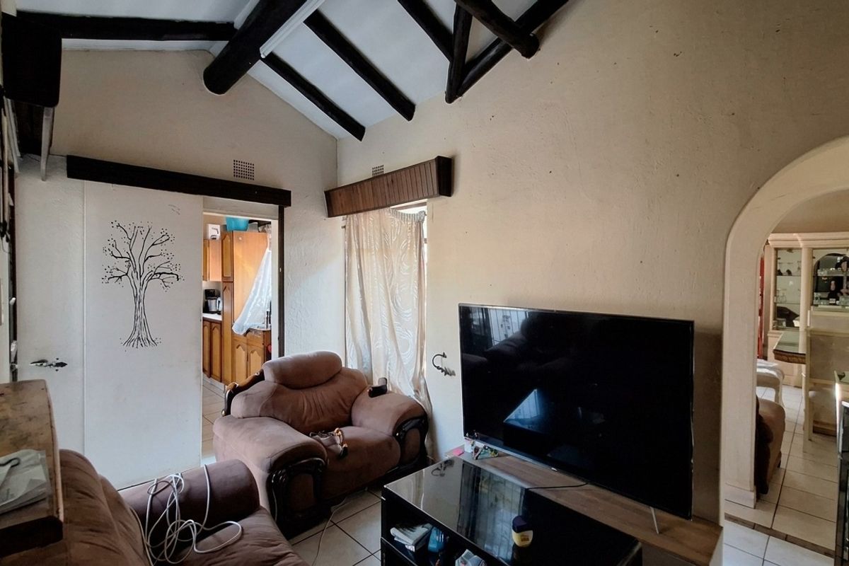 Living room featuring a vaulted ceiling with exposed timber beams, tiled flooring, and an arched entryway leading to adjacent living spaces.