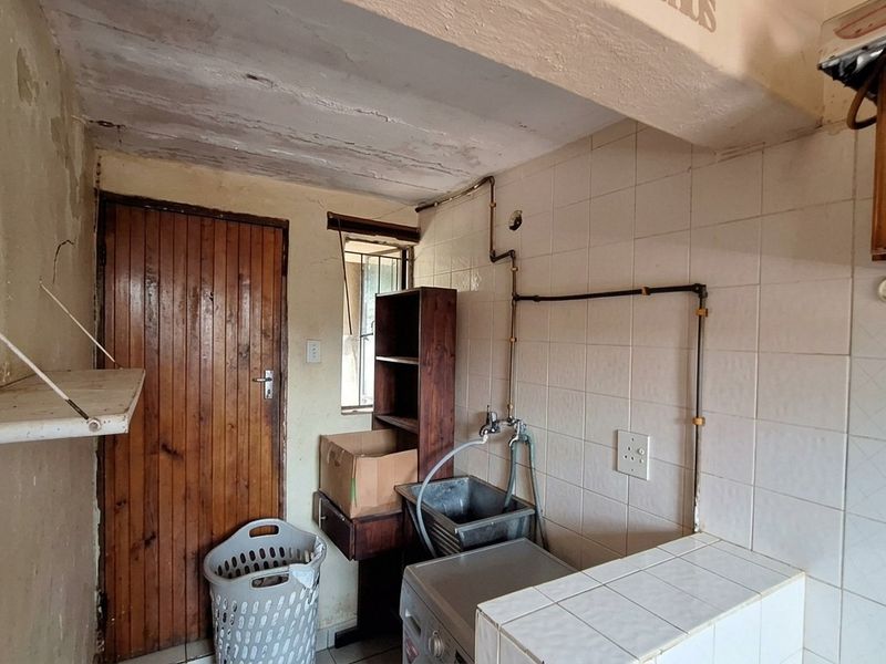 A functional laundry area featuring a utility sink, tiled splashback, and exposed plumbing, requiring maintenance and cosmetic updates to improve its overall condition.