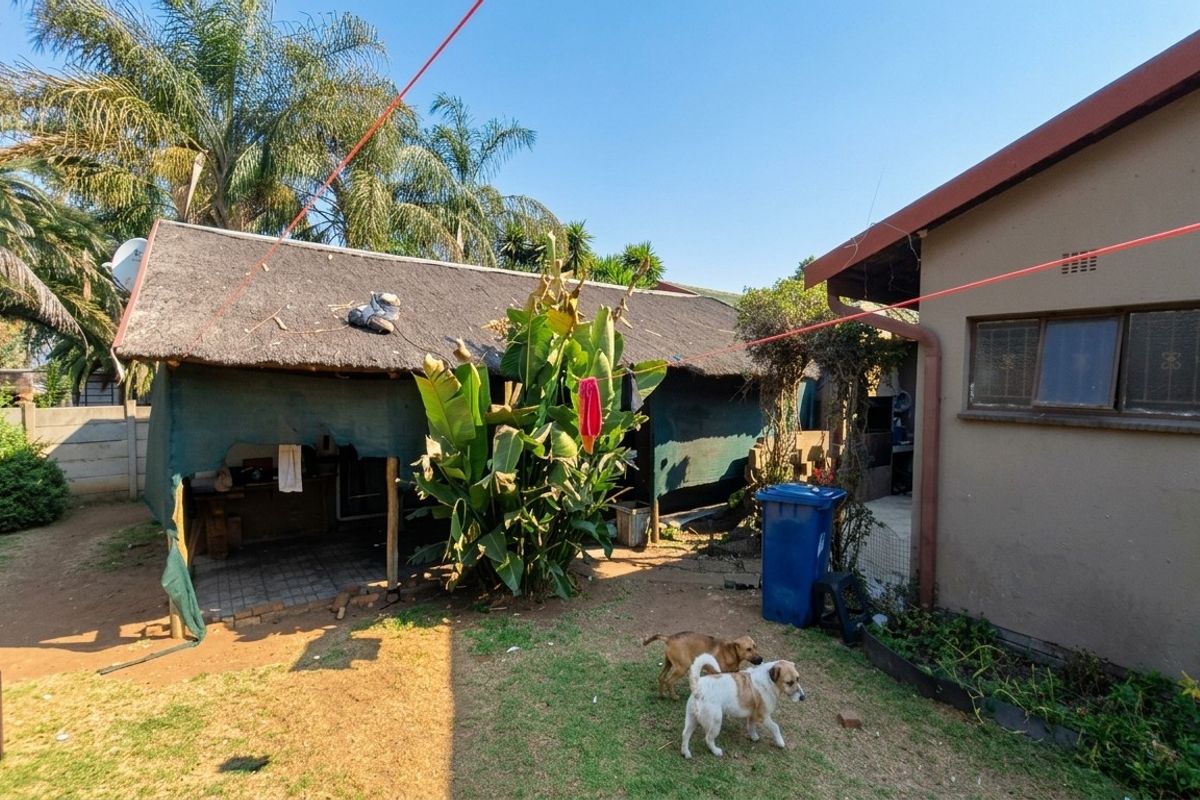 Rear garden area featuring a thatched outdoor structure, concrete boundary wall, and paved patio space adjacent to the main house.