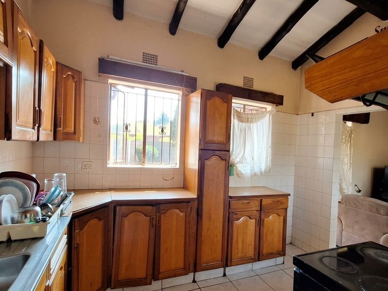 A functional kitchen featuring wooden cabinetry, tiled backsplash, and exposed timber ceiling beams, offering a traditional aesthetic with potential for modern updates.