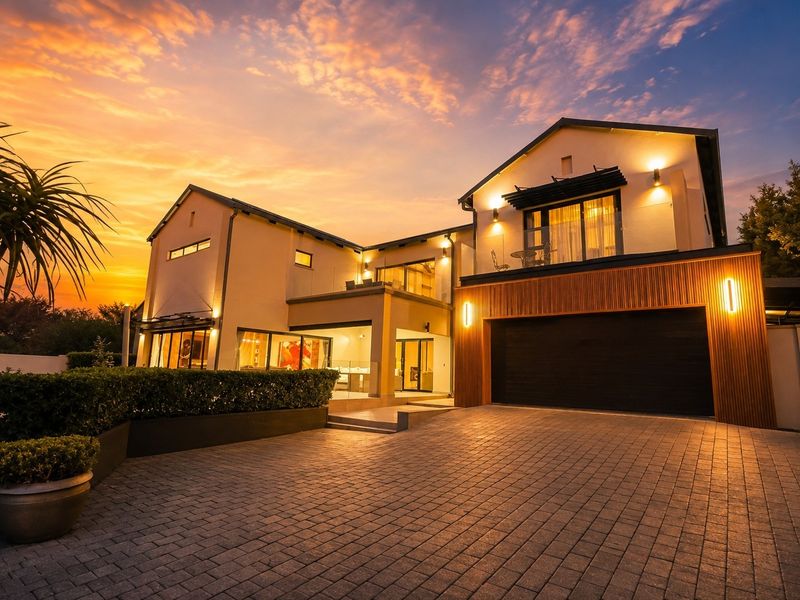 Modern double-story residence featuring a paved driveway, integrated double garage with timber accents, and an upper-level balcony at sunset.