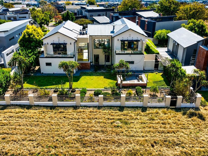 Aerial view of a modern residential property featuring a metal roof, landscaped garden, and a rear patio area with glass-balustraded balconies.