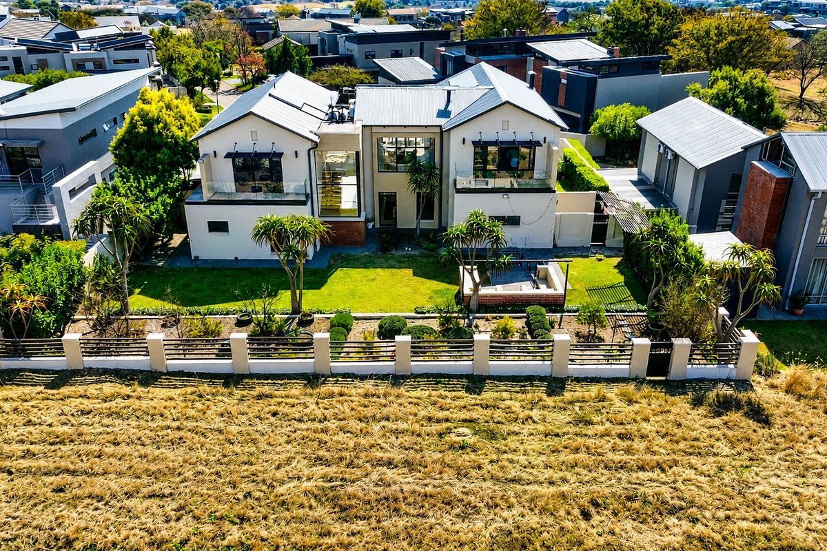 Aerial view of a modern residential property featuring a metal roof, landscaped garden, and a rear patio area with glass-balustraded balconies.