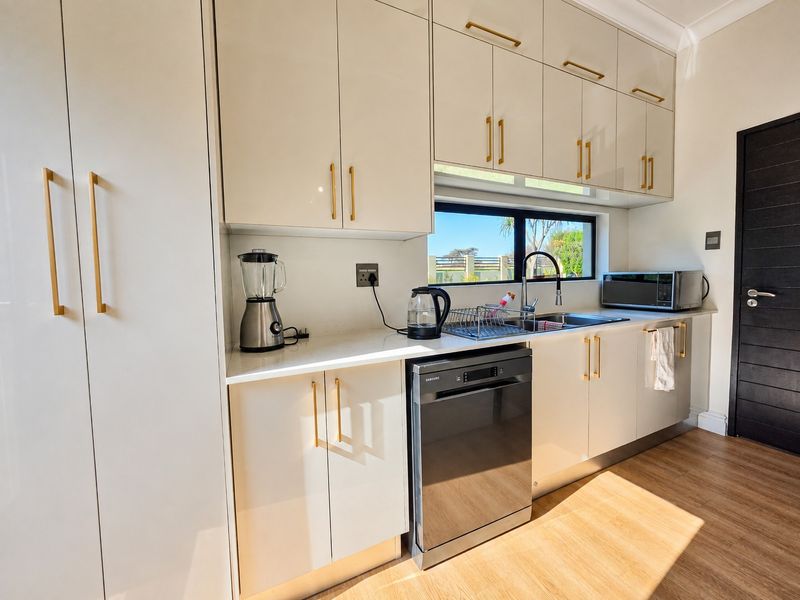 Modern kitchen featuring high-gloss cabinetry, gold hardware, quartz countertops, integrated dishwasher, and a sleek undermount sink with a gooseneck faucet.