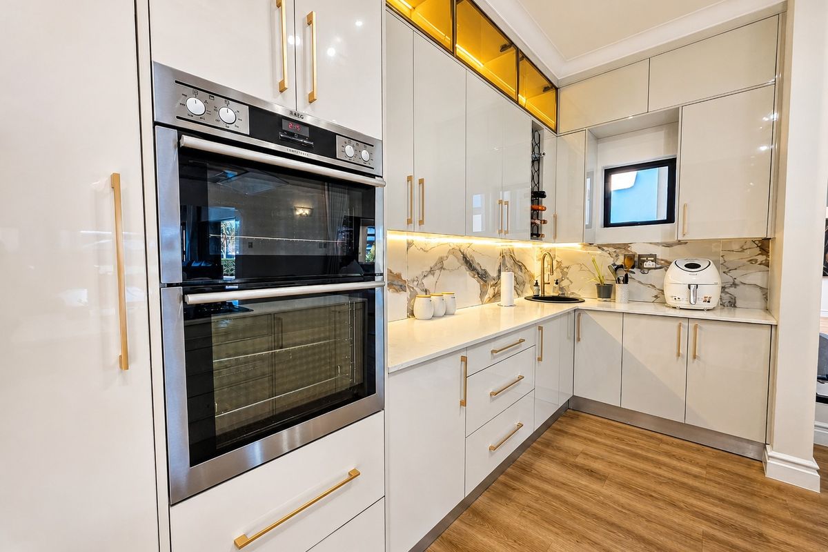 Modern kitchen featuring high-gloss cabinetry, built-in double oven, stone countertops, marble-look backsplash, and warm under-cabinet lighting.