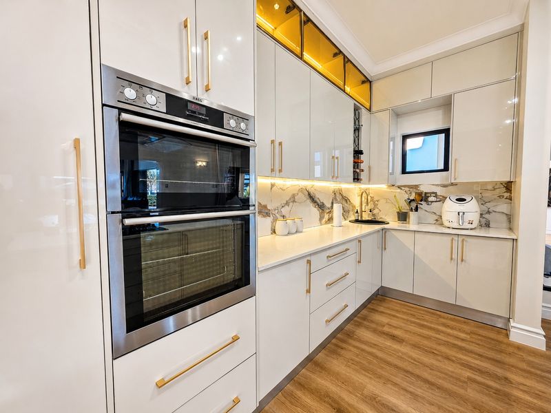 Modern kitchen featuring high-gloss cabinetry, built-in double oven, stone countertops, marble-look backsplash, and warm under-cabinet lighting.