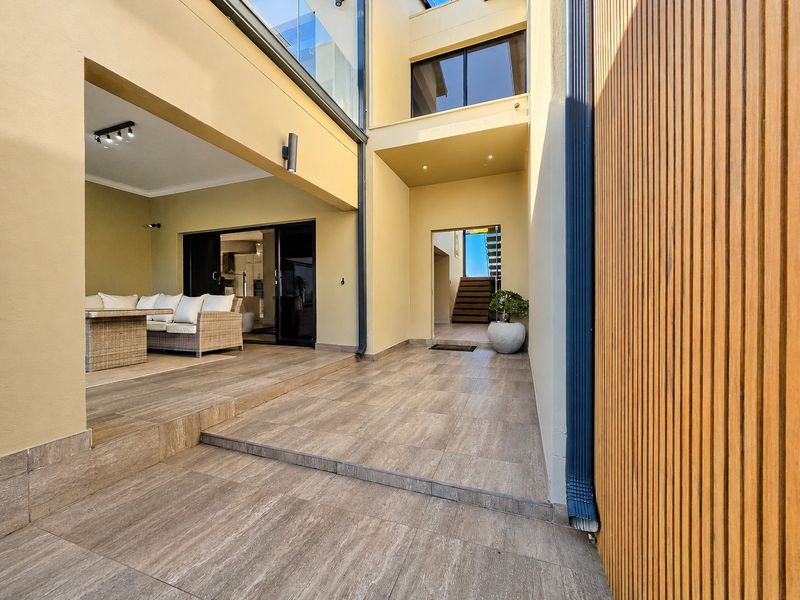A modern, covered patio area featuring wood-look tiled flooring, timber slat wall detailing, and seamless access to the interior living space.