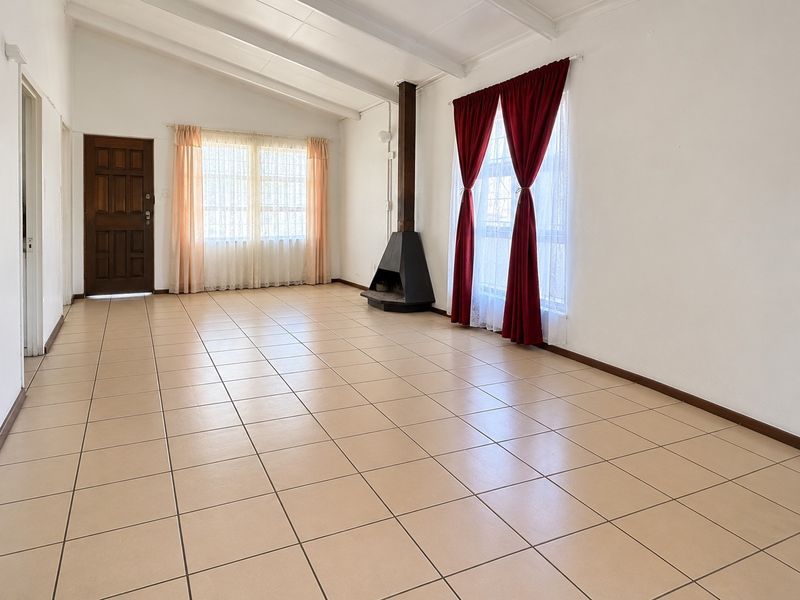 Spacious living area featuring neutral tiled flooring, exposed beam ceilings, and a central freestanding fireplace, offering a bright and versatile blank canvas.