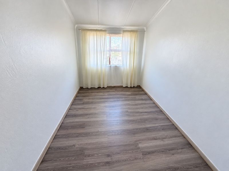 A bright, empty bedroom featuring modern laminate wood-look flooring and neutral white walls, ready for personalization.