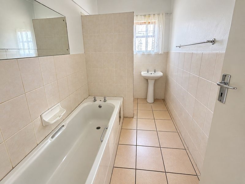 A clean, functional bathroom featuring a bathtub, pedestal basin, and neutral floor-to-ceiling wall tiling.
