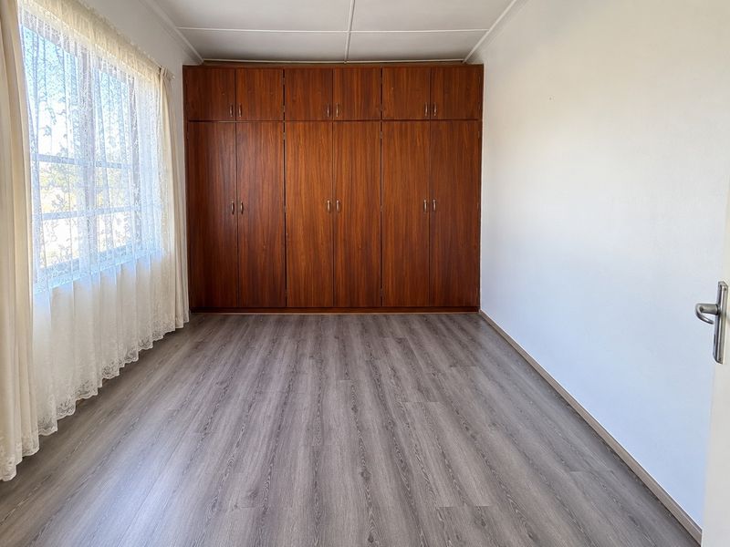 A clean, empty bedroom featuring modern grey laminate flooring and extensive floor-to-ceiling built-in wooden cupboards.