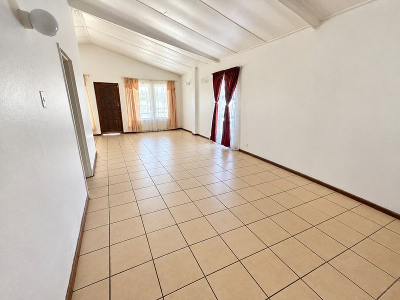 Spacious living area featuring vaulted ceilings, neutral ceramic tile flooring, and direct access to the exterior through a glass sliding door.
