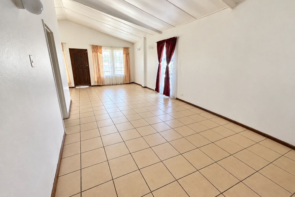 Spacious living area featuring vaulted ceilings, neutral ceramic tile flooring, and direct access to the exterior through a glass sliding door.