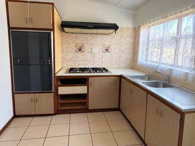 A dated kitchen featuring built-in cabinetry, a gas hob with extractor fan, built-in oven, and a double stainless steel sink with tiled splashbacks.