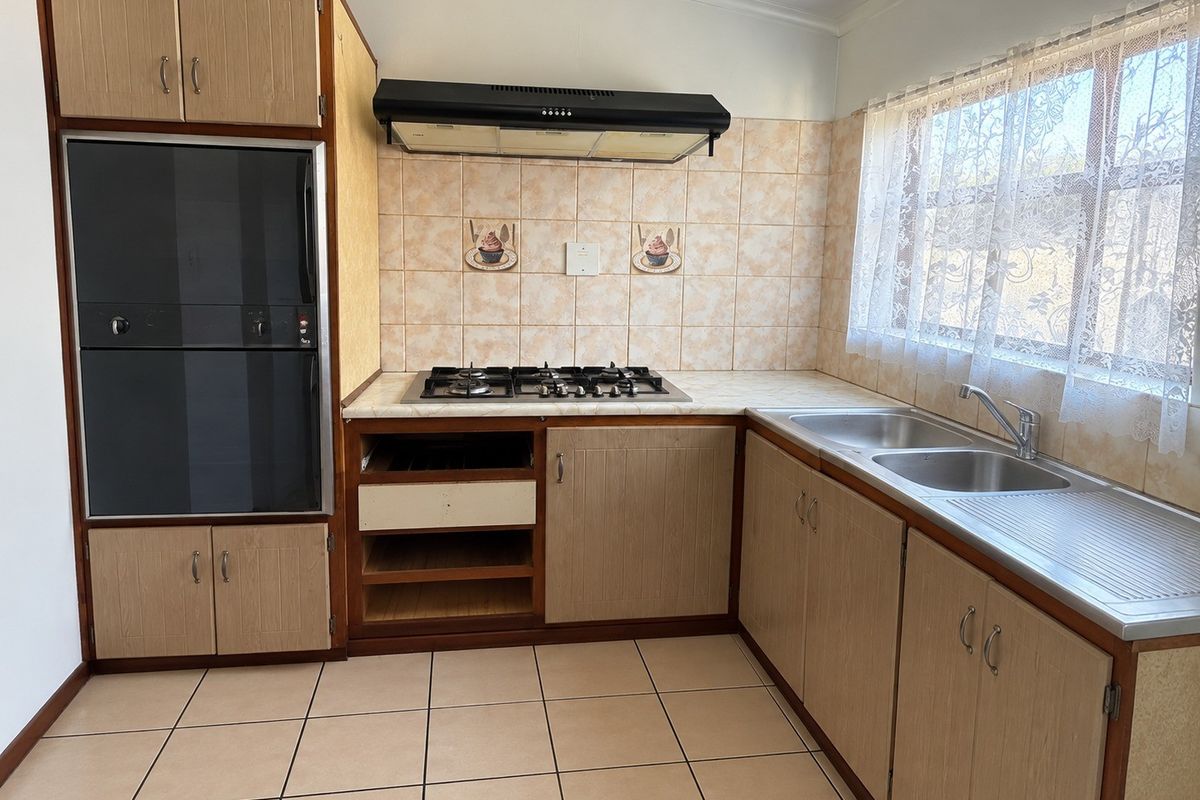A dated kitchen featuring built-in cabinetry, a gas hob with extractor fan, built-in oven, and a double stainless steel sink with tiled splashbacks.