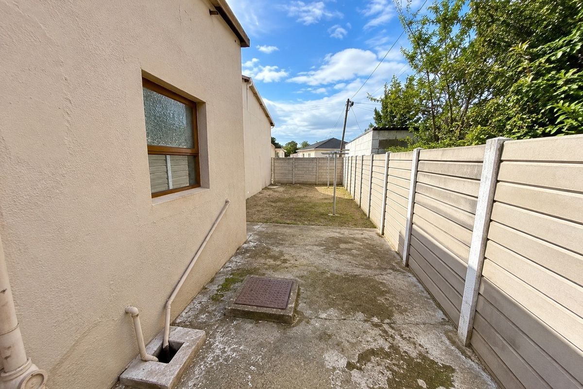 A rear exterior view featuring a concrete patio area, precast boundary wall, and small garden space with external plumbing fixtures.