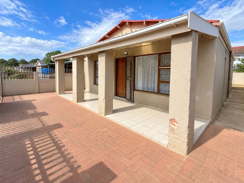 A covered patio area featuring tiled flooring and concrete pillars, leading to a paved outdoor space with boundary walling.