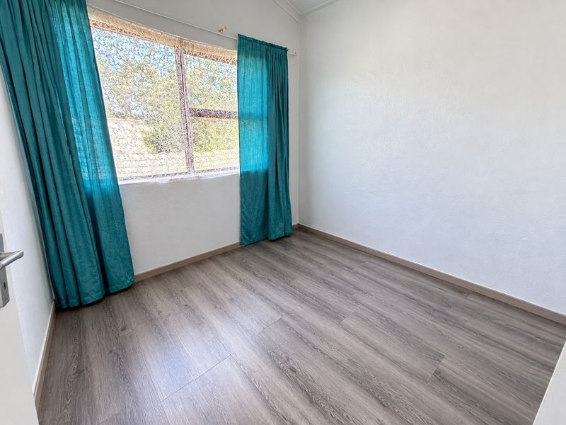 A bright, empty bedroom featuring modern grey laminate flooring and neutral white walls, ready for personalization.