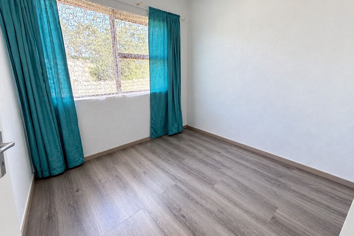 A bright, empty bedroom featuring modern grey laminate flooring and neutral white walls, ready for personalization.