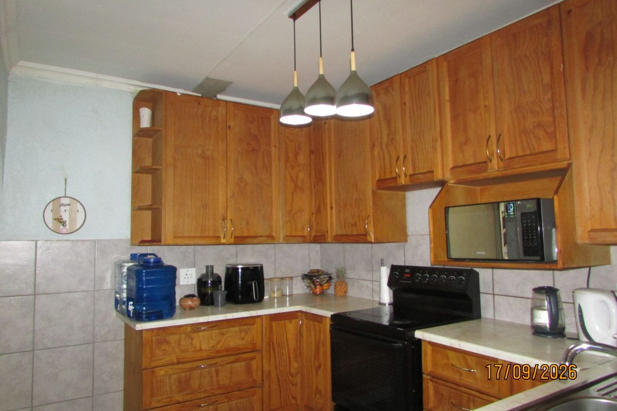 A functional kitchen featuring wooden cabinetry, tiled backsplash, laminate countertops, and integrated appliances including a built-in microwave and stove.