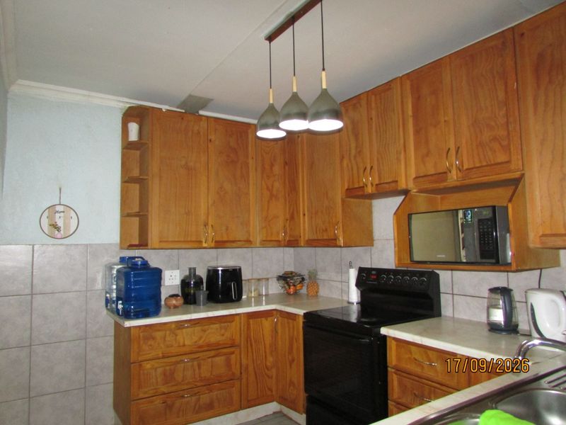 A functional kitchen featuring wooden cabinetry, tiled backsplash, laminate countertops, and integrated appliances including a built-in microwave and stove.