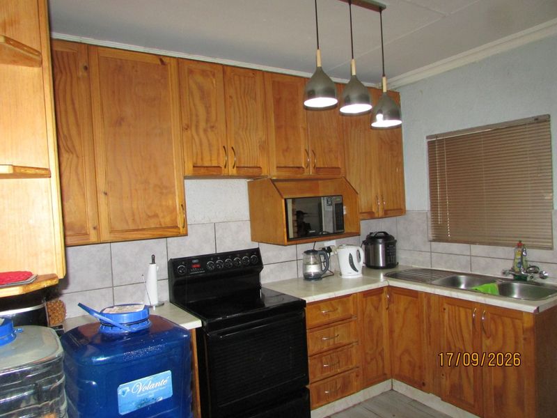 A functional kitchen featuring wooden cabinetry, tiled backsplash, and a stainless steel sink, offering a classic layout with potential for modern updates.