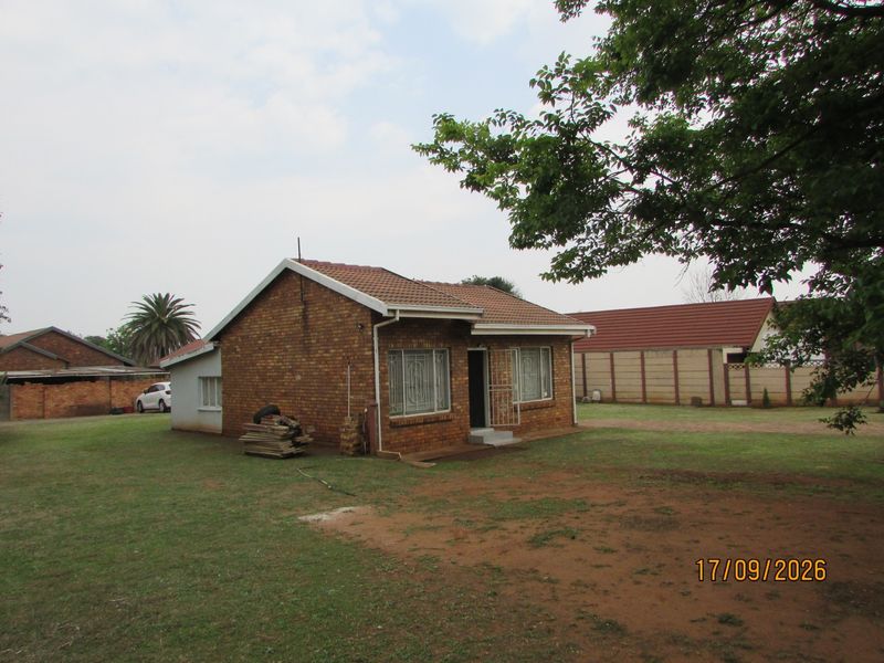 A detached face brick house featuring a tiled roof, security bars on windows, and a large surrounding garden area with perimeter walling.