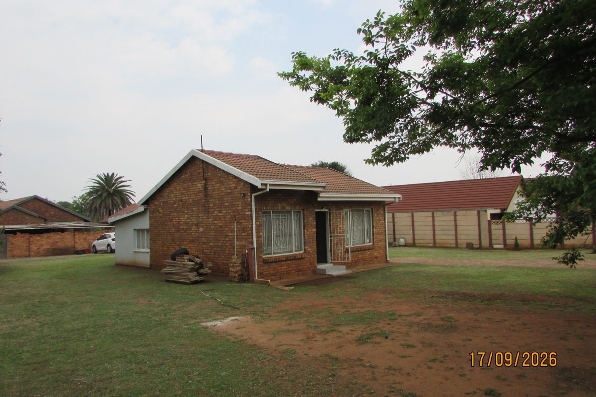 A detached face brick house featuring a tiled roof, security bars on windows, and a large surrounding garden area with perimeter walling.