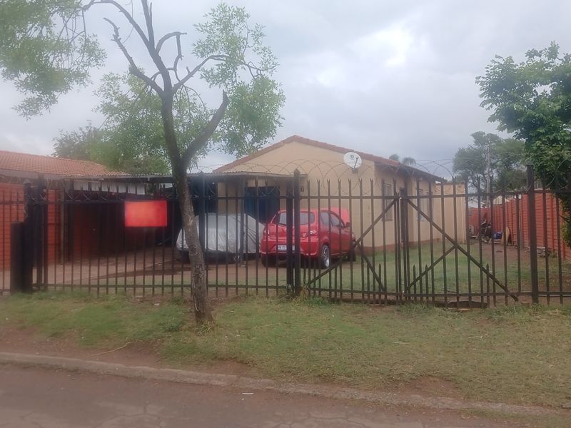 Front view of a single-story house featuring a secure metal perimeter fence, gated driveway, and tiled roof.