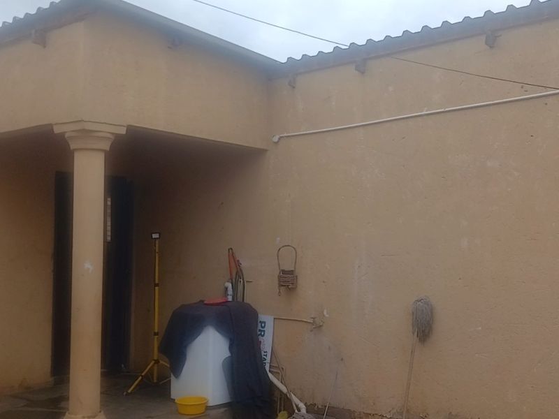 A rear exterior view of the property featuring a covered patio area with a concrete column and weathered wall finishes.