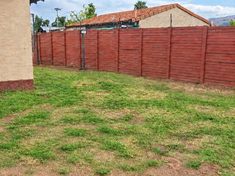 A rear garden area featuring a brick exterior wall and a perimeter timber fence with security wire.