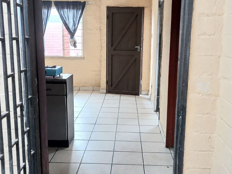 A functional hallway featuring tiled flooring, exposed brick walls, and a secure entrance gate, leading to internal rooms.