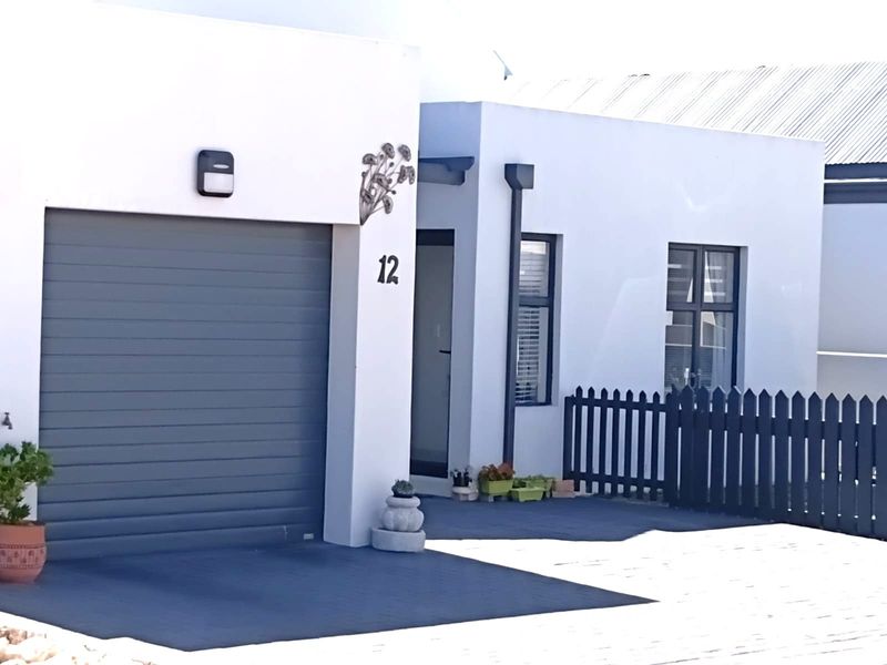 Front elevation of a modern house featuring a single garage, paved driveway, and a dark picket fence.