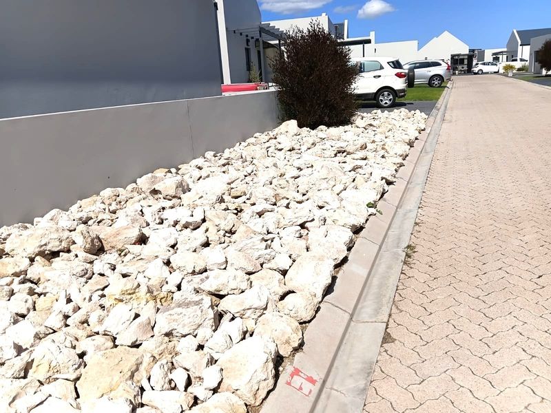 A view of the property's street-facing exterior, featuring a paved driveway, concrete kerbing, and a decorative rock garden.