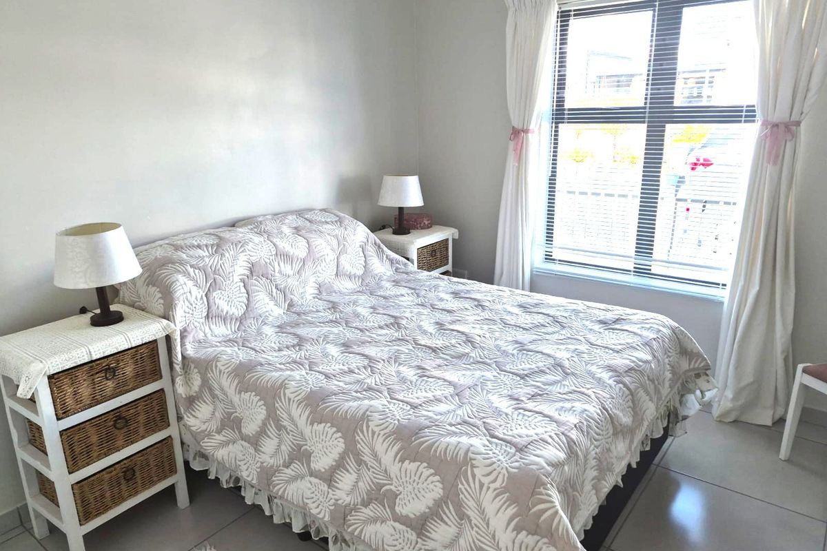 A bright bedroom featuring neutral tiled flooring and a large window with venetian blinds, offering a clean and functional living space.
