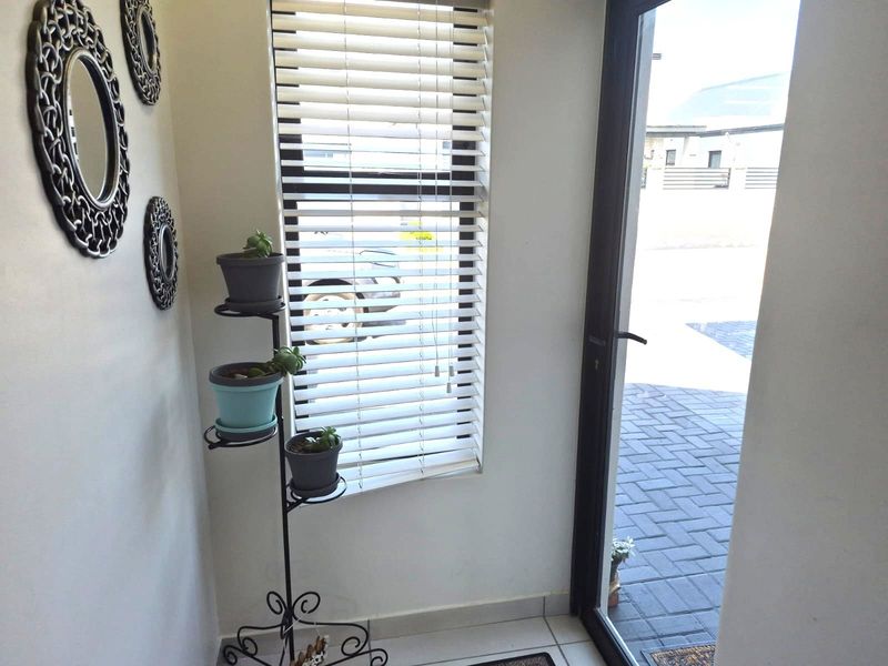 A bright entrance area featuring tiled flooring, a modern aluminium door frame, and venetian blinds allowing natural light into the space.