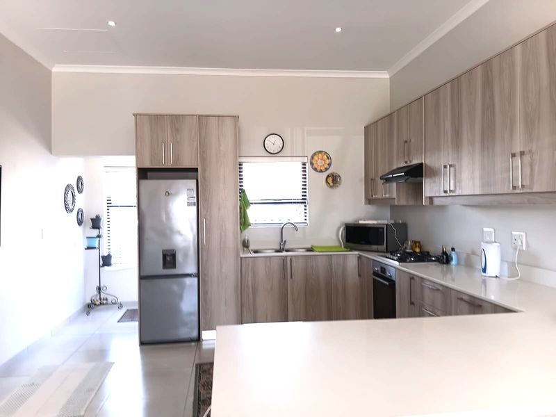 Modern kitchen featuring light wood-grain cabinetry, stone countertops, integrated appliances, and recessed downlighting, offering a clean and functional workspace.