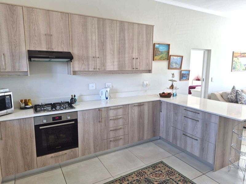 Modern kitchen featuring light wood-grain cabinetry, stone countertops, a gas hob, and a built-in oven, offering a clean and functional cooking space.