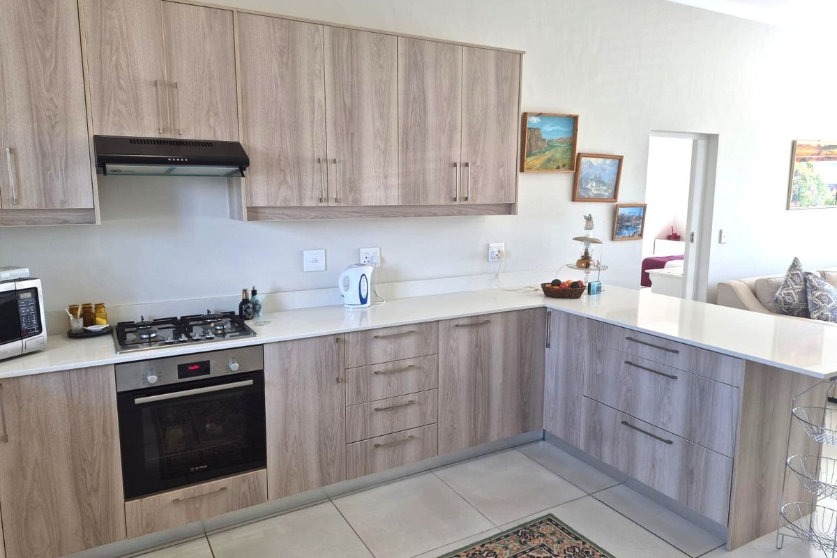 Modern kitchen featuring light wood-grain cabinetry, stone countertops, a gas hob, and a built-in oven, offering a clean and functional cooking space.