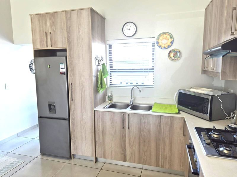 Modern kitchen featuring light wood-look cabinetry, a double basin sink, gas hob, built-in oven, and tiled flooring.
