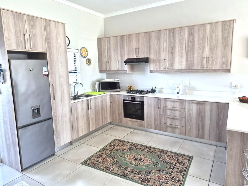 Modern kitchen featuring light wood-grain cabinetry, white countertops, built-in oven, gas hob, extractor fan, and neutral tiled flooring.