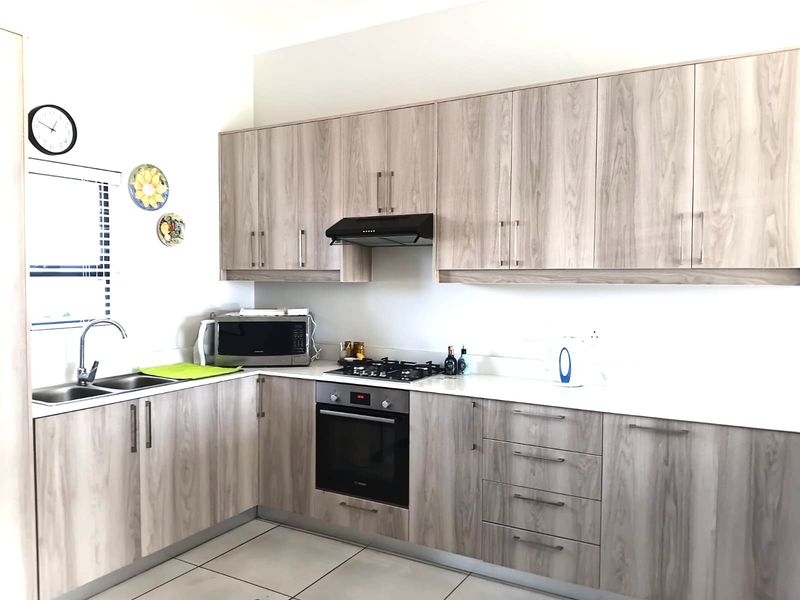Modern kitchen featuring light wood-grain cabinetry, stone countertops, built-in oven, gas hob, and stainless steel sink with tiled flooring.