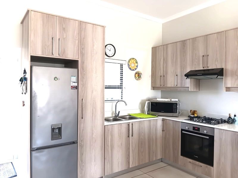 Modern kitchen featuring light wood-grain cabinetry, integrated gas cooktop, built-in oven, extractor fan, and double sink with tiled flooring.