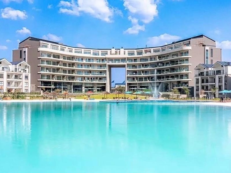 A wide-angle view of a large, modern apartment complex featuring a central swimming pool and landscaped outdoor area.