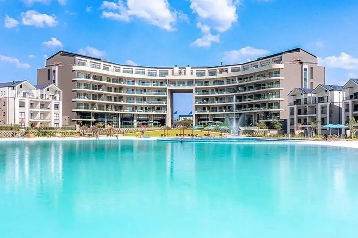 A wide-angle view of a large, modern apartment complex featuring a central swimming pool and landscaped outdoor area.