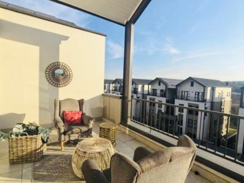 A spacious covered balcony featuring tiled flooring and a metal balustrade, offering pleasant views of the surrounding residential complex.