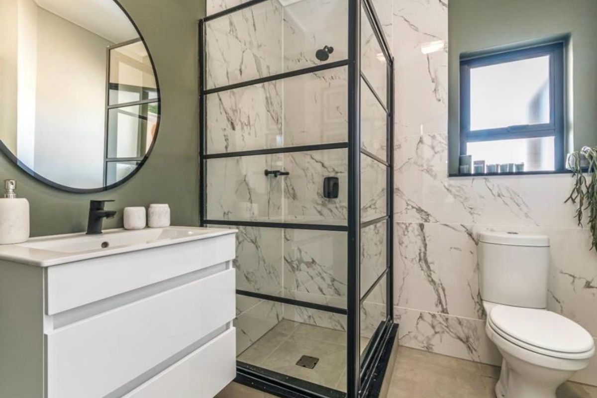 Modern bathroom featuring a sleek vanity, marble-look wall tiles, and a contemporary black-framed shower enclosure.
